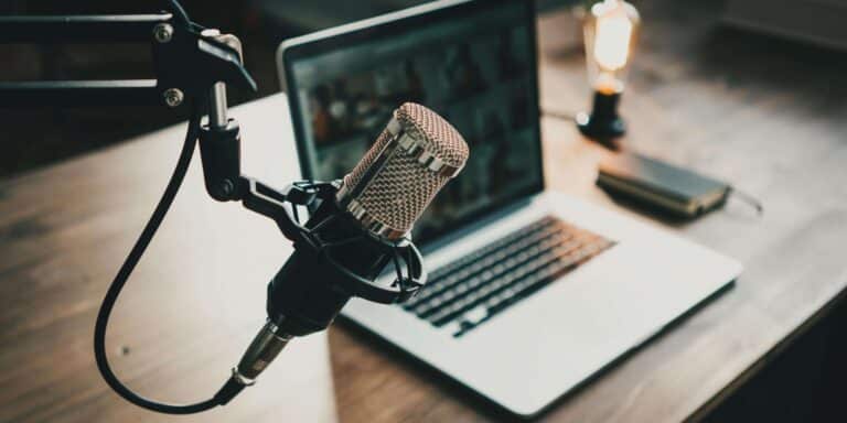 Podcast microphone beside laptop and notebook on desk.