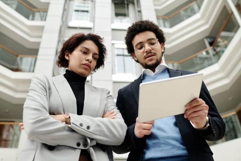 Colleagues discussing work on tablet in modern building.