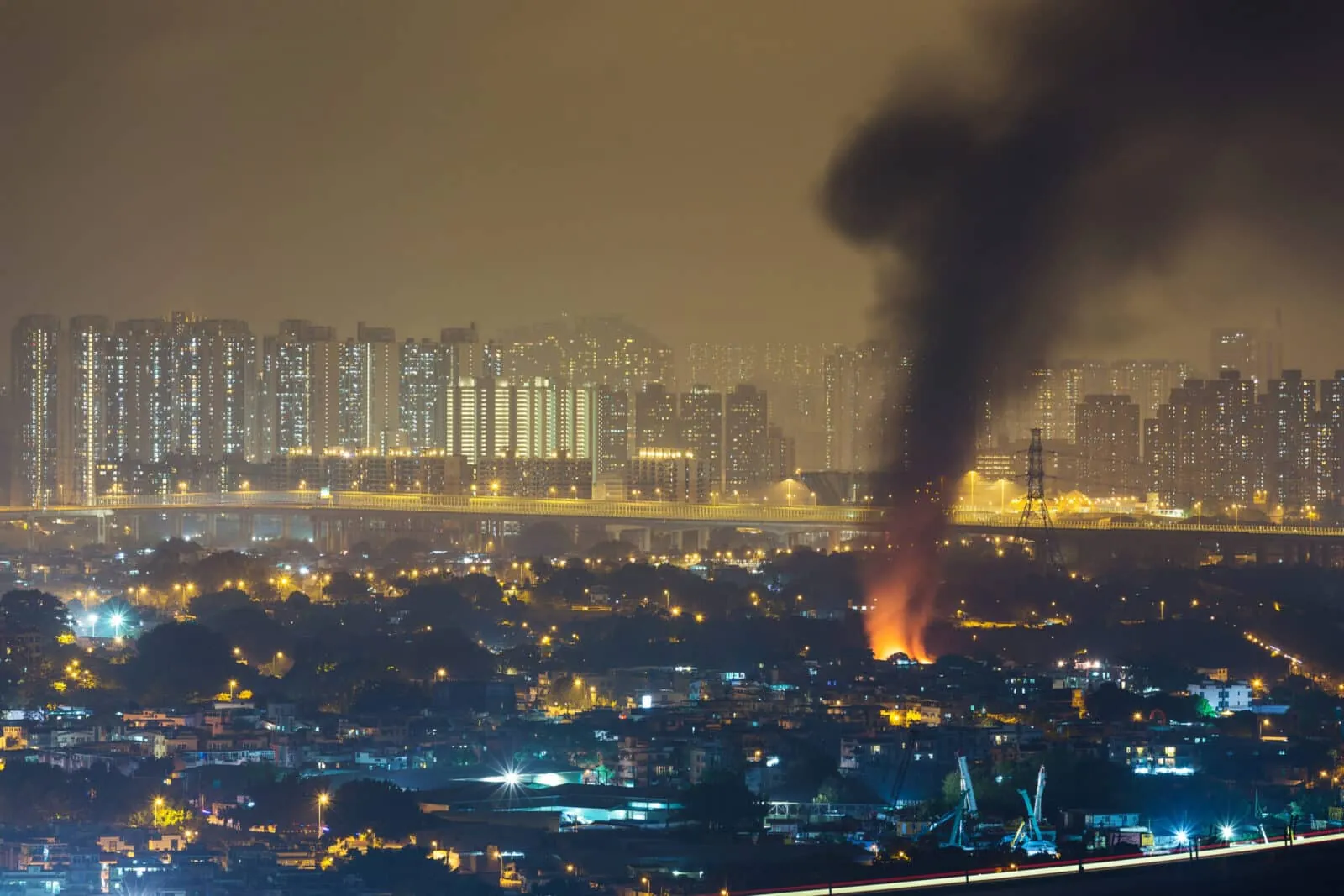 Cityscape with smoke rising from fire at night.