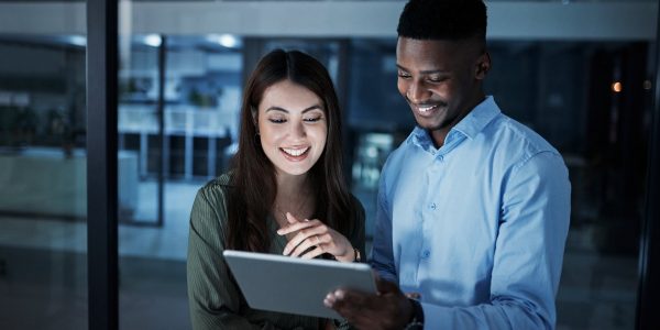 Shot of two businesspeople discussing something on a digital tablet in an office at night